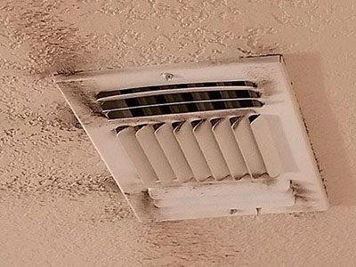 ceiling vent with visible dust and dirt on a beige colored ceiling.