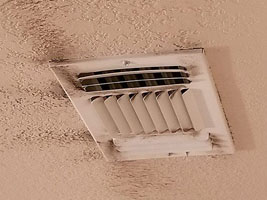 A ceiling vent with visible dust and dirt on a beige colored ceiling